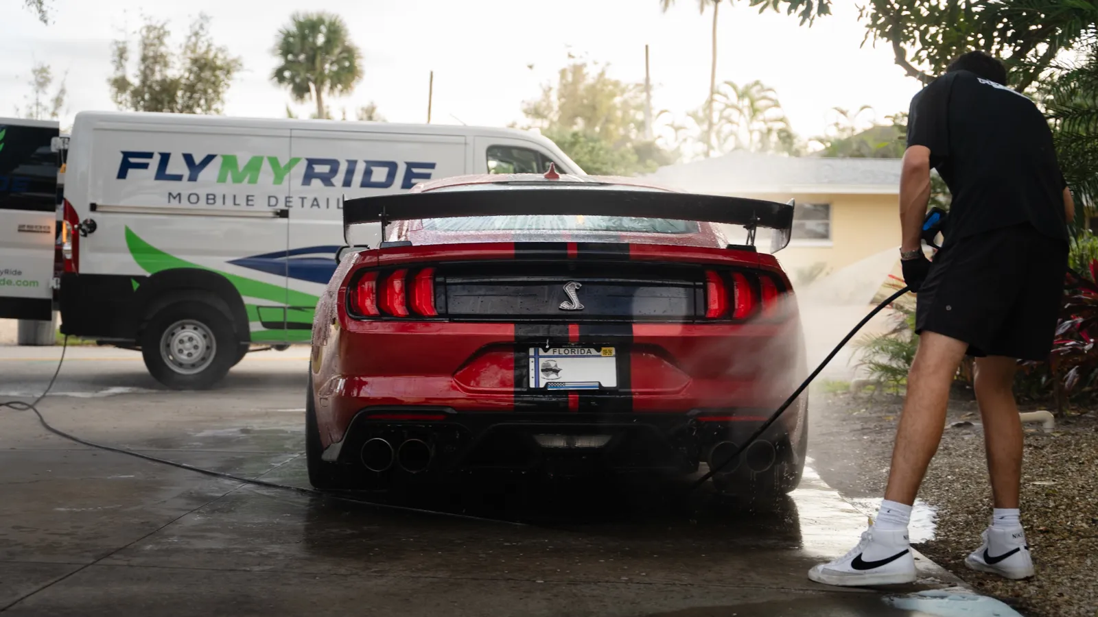 Man with hands in pockets stands in front of a vintage cream car on a forest road in daylight
