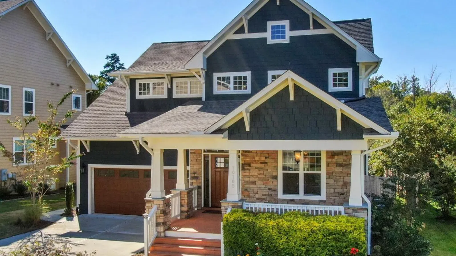 White coastal home with wraparound porch and manicured lawn under clear sky in Gainesville