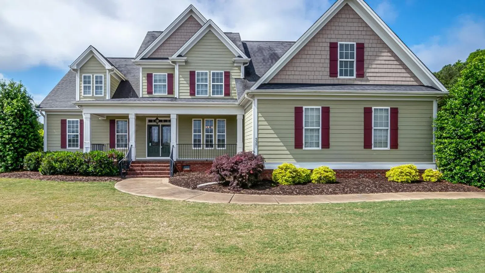 White coastal home with wraparound porch and manicured lawn under clear sky in Peachtree Corners