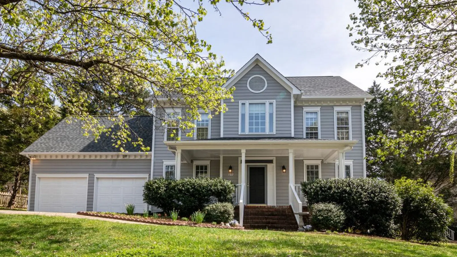 White coastal home with wraparound porch and manicured lawn under clear sky in Johns Creek
