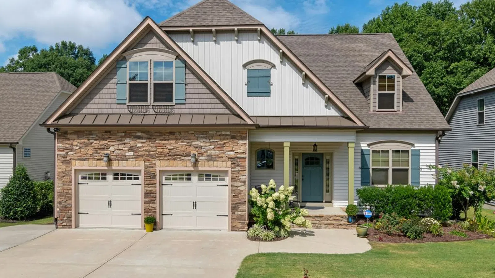 White coastal home with wraparound porch and manicured lawn under clear sky in Suwanee, GA