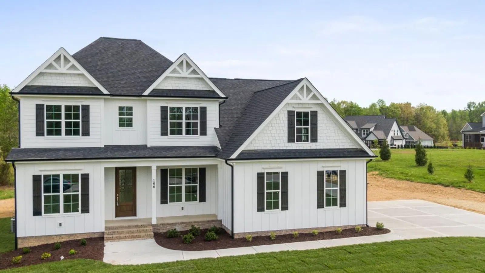 Modern two-story white farmhouse with black shutters, large windows, and a spacious front yard