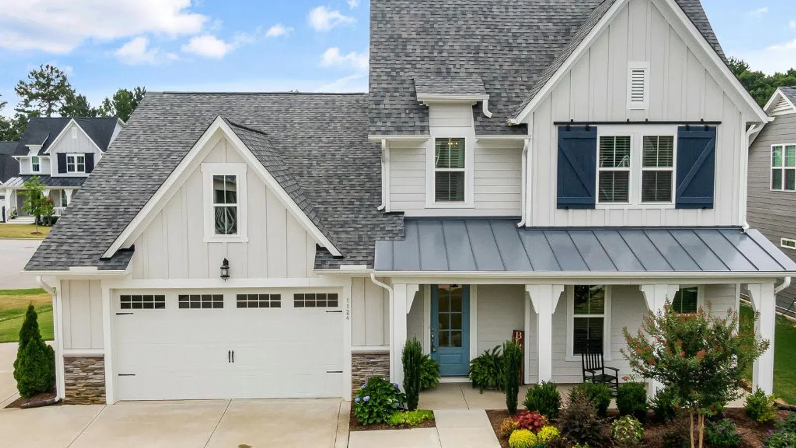 White coastal home with wraparound porch and manicured lawn under clear sky in Sugar Hill, GA