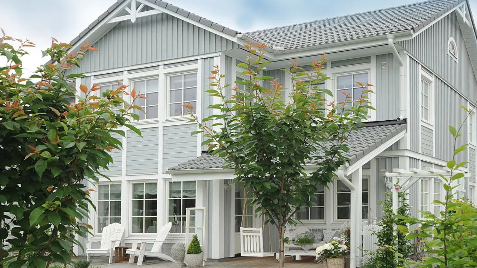 White coastal home with wraparound porch and manicured lawn under clear sky in Flowery Branch, GA