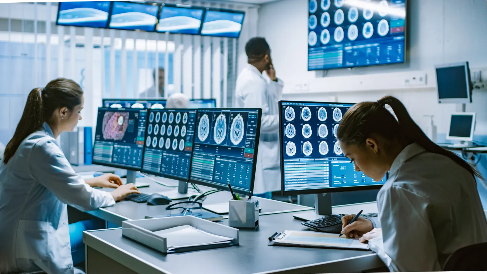 Medical professionals analyzing brain MRI scans on multiple computer screens in a modern clinical setting.