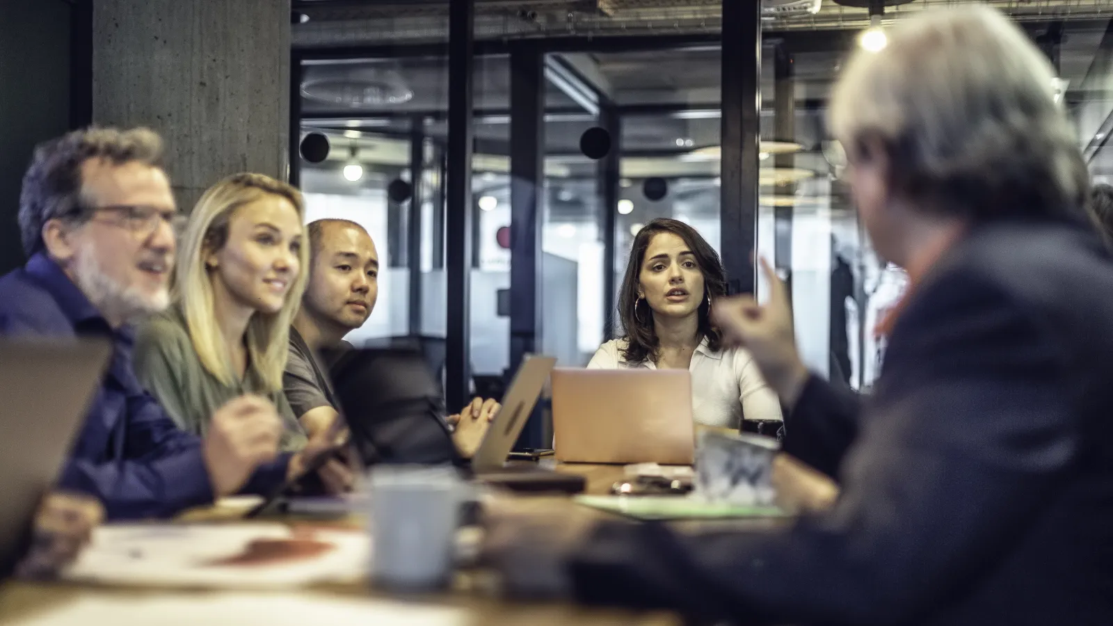 Team of five professionals engaged in a business meeting inside a modern office with laptops and documents.