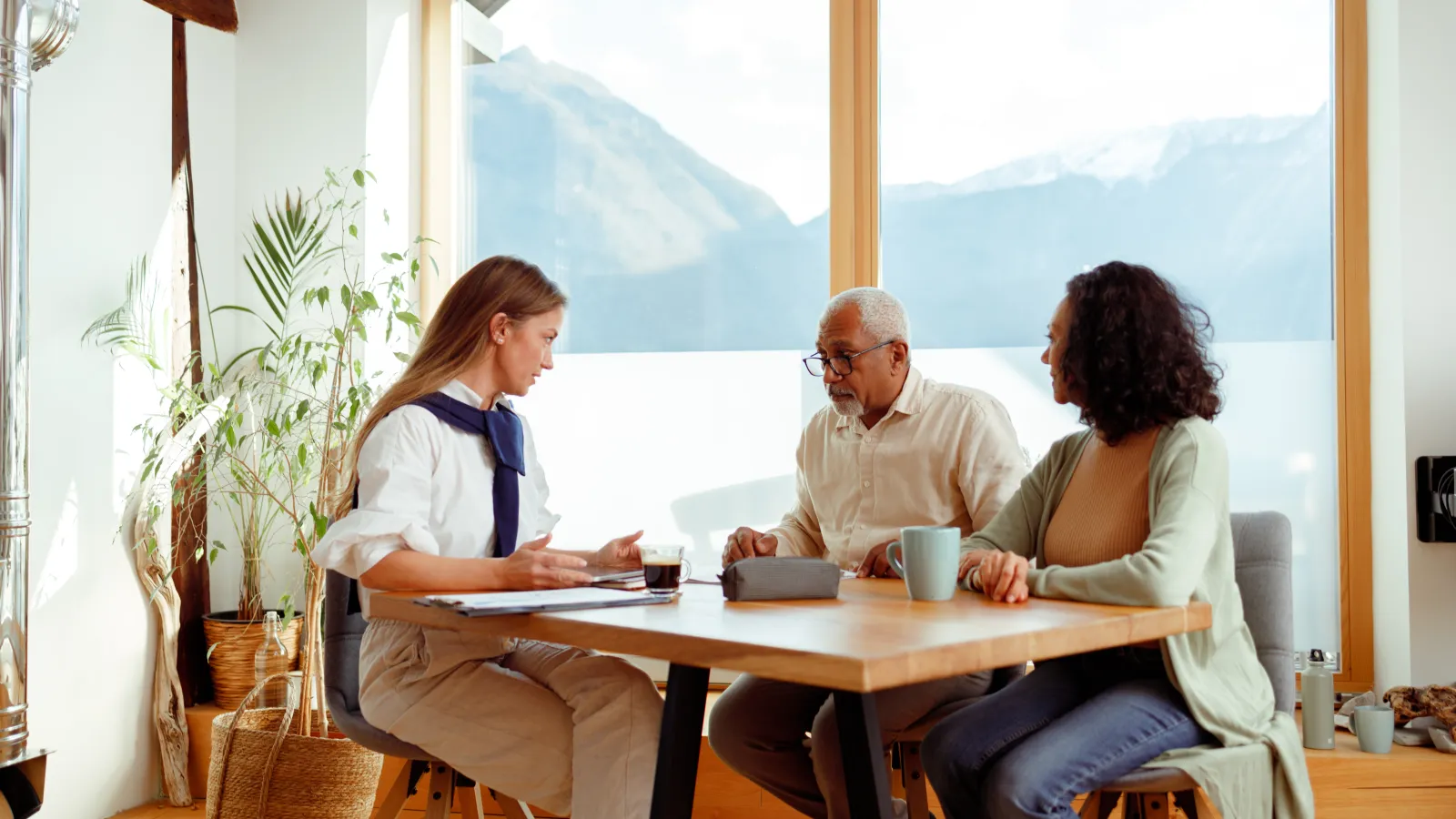 Financial advisor consulting senior couple at wooden table in bright modern home with mountain view