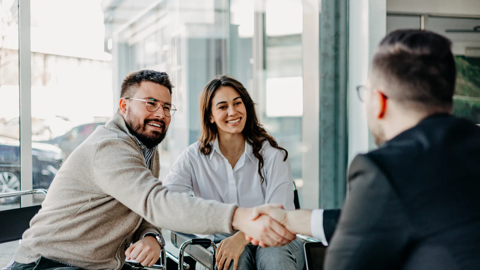 Young couple shaking hands with a man in a business setting during a meeting in a modern office.