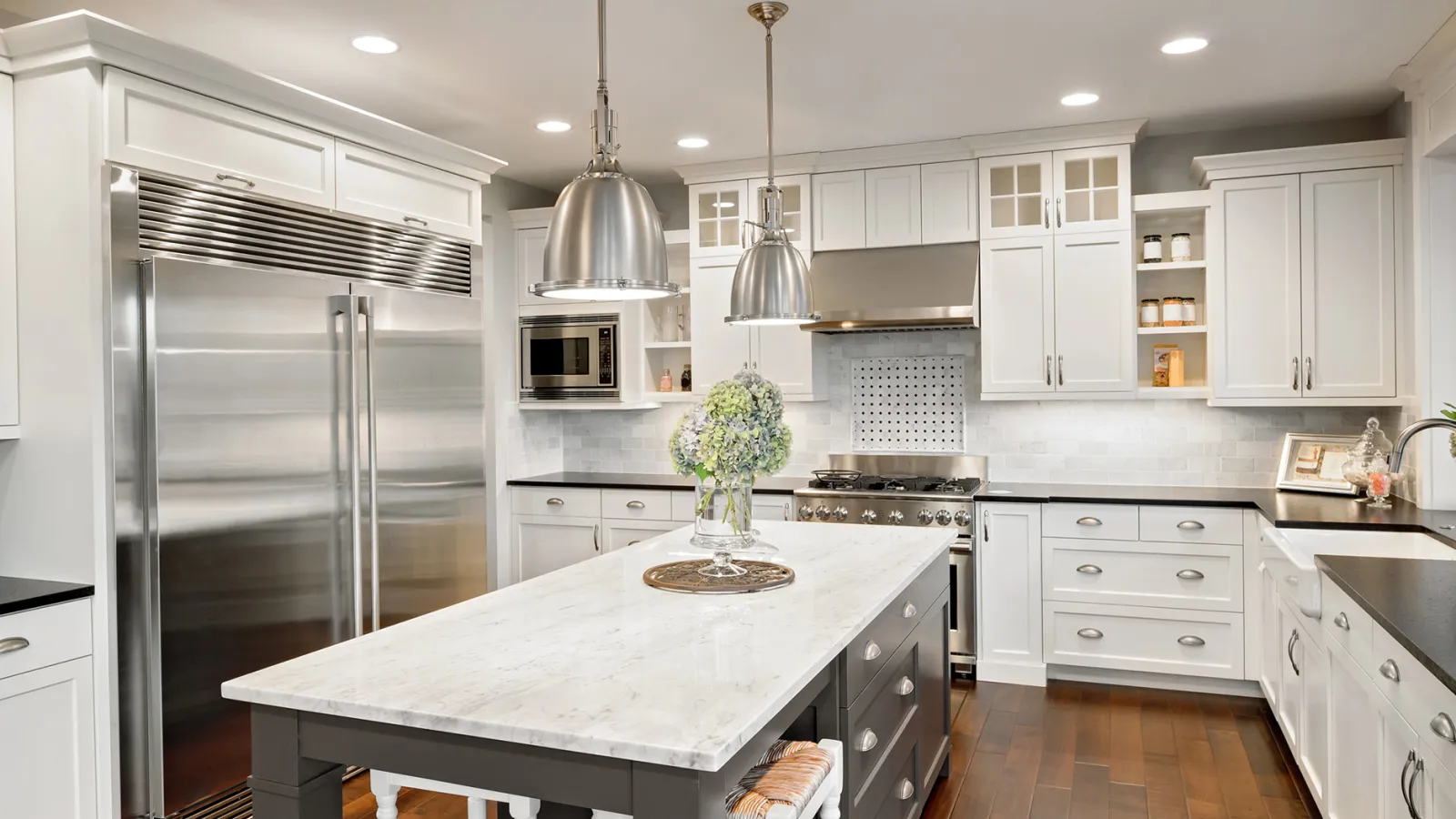 Modern kitchen with white cabinets, marble island, stainless steel appliances, and hardwood floors under bright lighting.