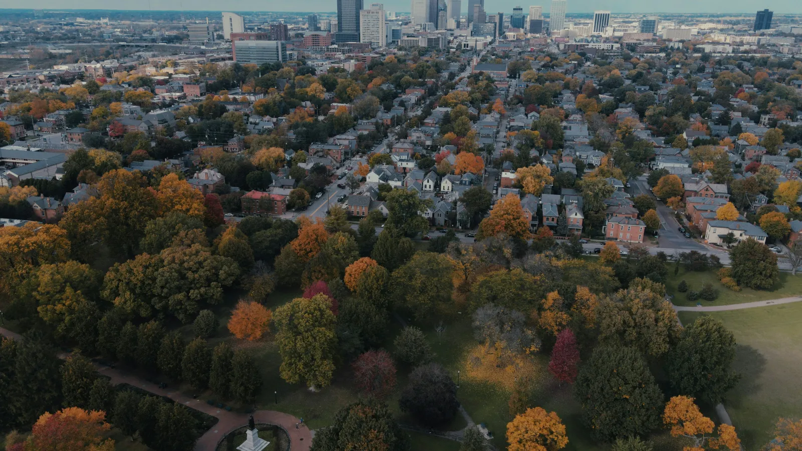 Aerial view of a city skyline with residential neighborhoods and colorful autumn trees in a park.