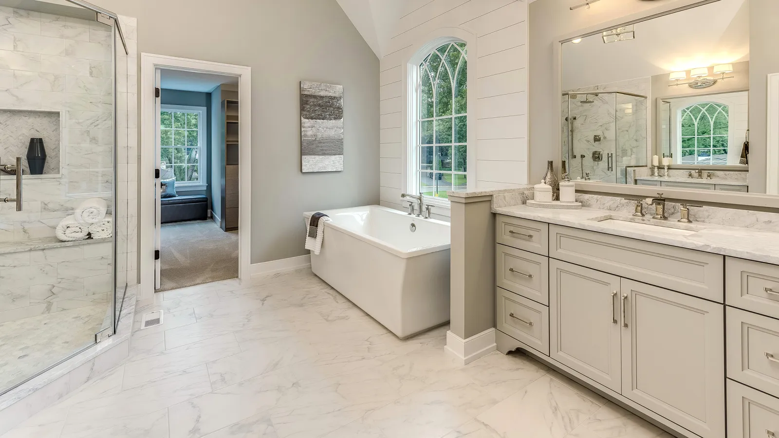 Bright modern bathroom with marble floors, glass shower, freestanding tub, and large vanity with mirror.