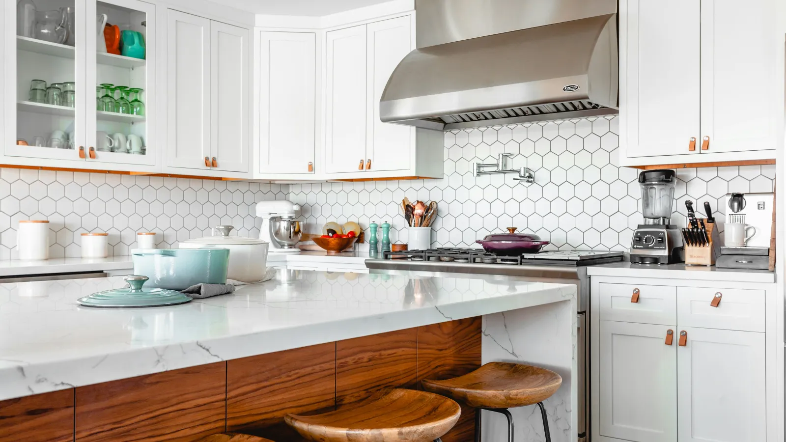 Modern kitchen with white cabinetry, hexagonal tile backsplash, wooden stools, and stainless steel appliances