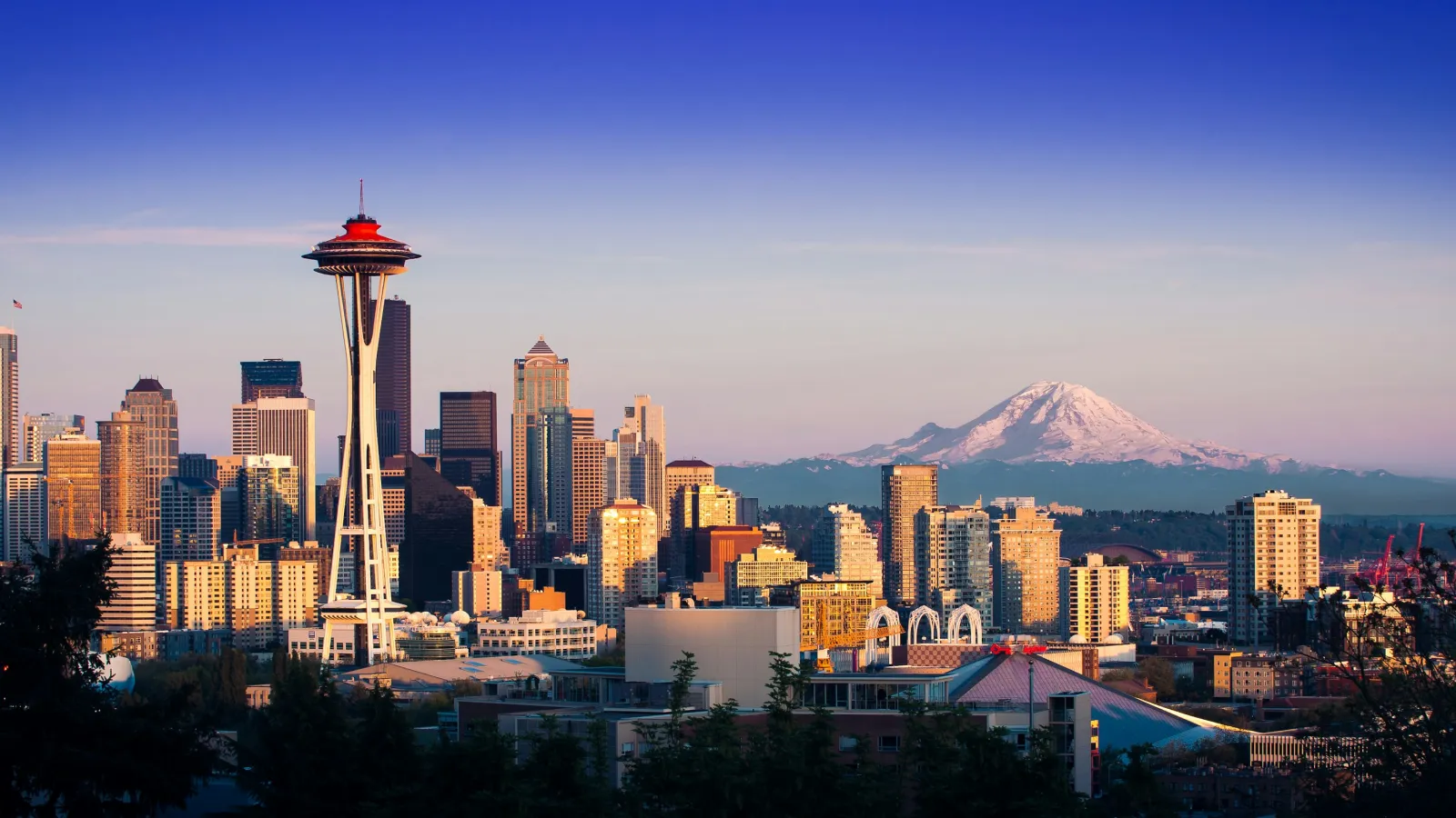 Seattle skyline at sunset with Space Needle and Mount Rainier in the background under clear sky