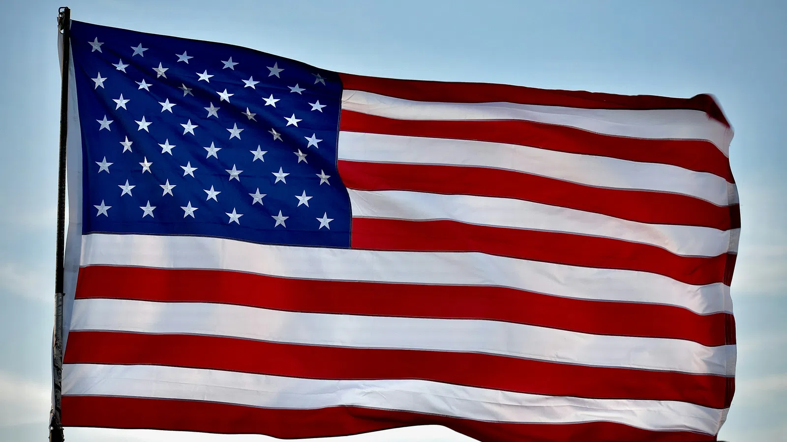American flag waving in the wind against a blue sky with white clouds, symbolizing patriotism.