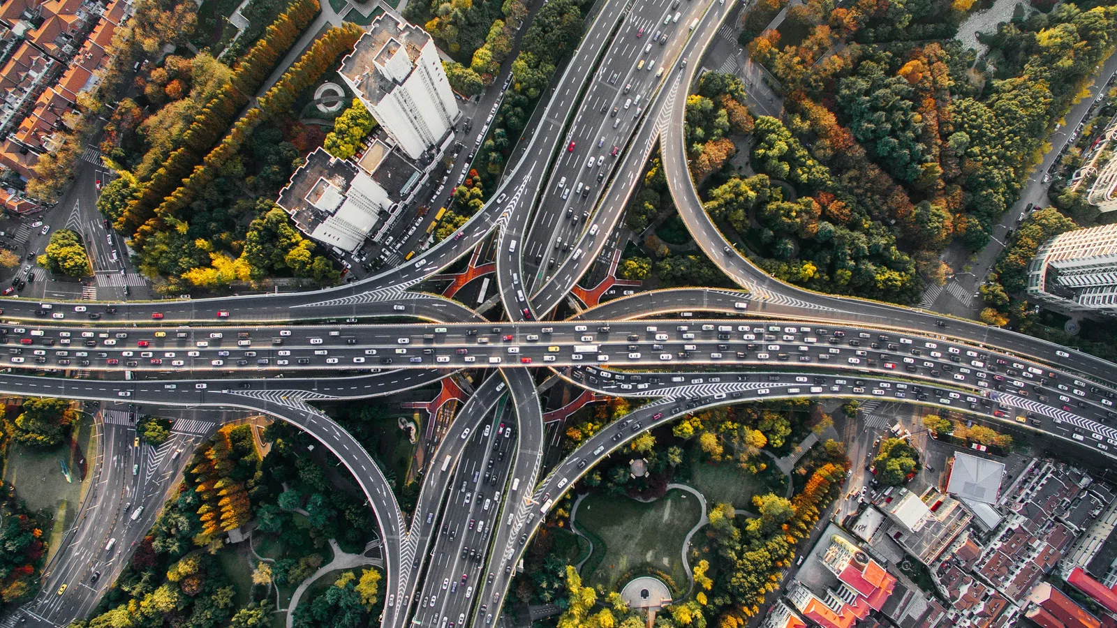 Aerial view of a busy multi-level highway interchange surrounded by buildings and green trees in autumn.