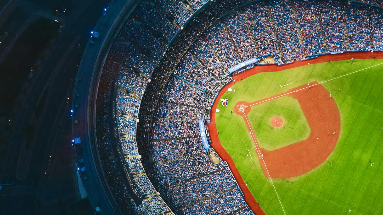 Aerial view of a packed baseball stadium with a brightly lit field and fans filling the stands at night.