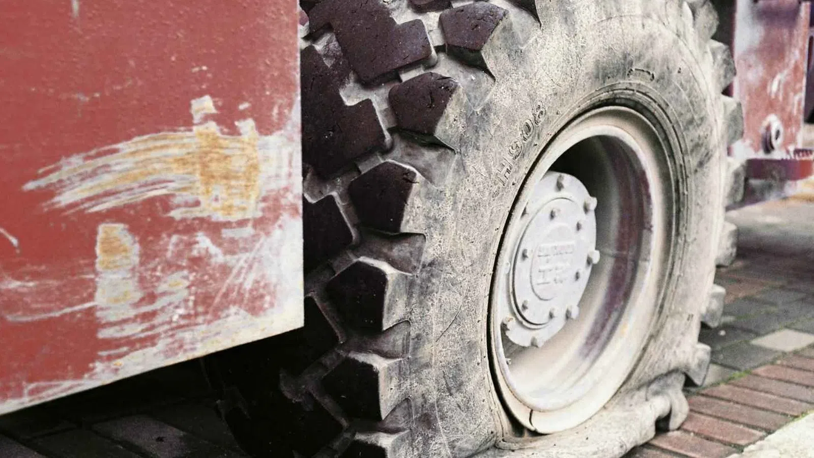 Close-up of a large flat tire on a rugged industrial vehicle with a worn red body and brick pavement.