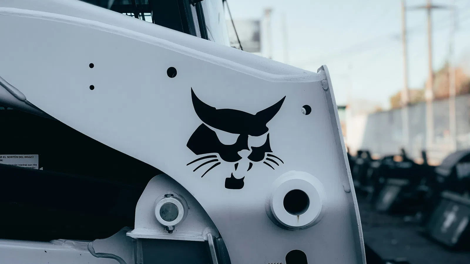 Close-up of a white construction vehicle featuring a black Bobcat logo on the side panel outdoors.