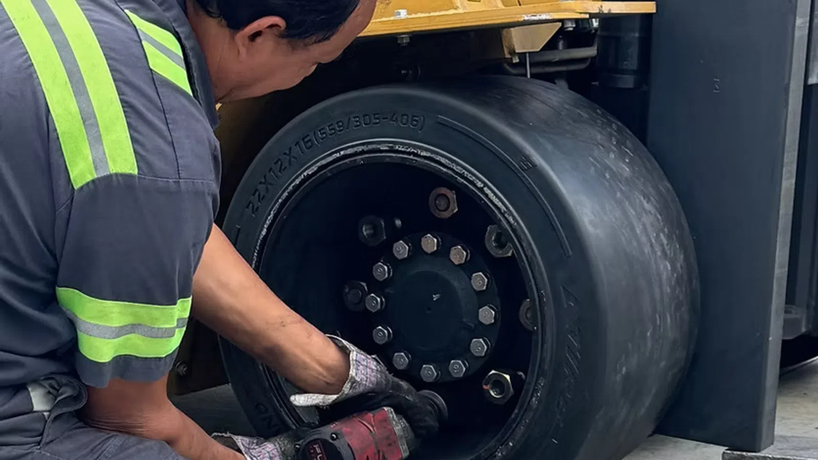 Worker using power tool to repair or maintain forklift wheel in industrial setting