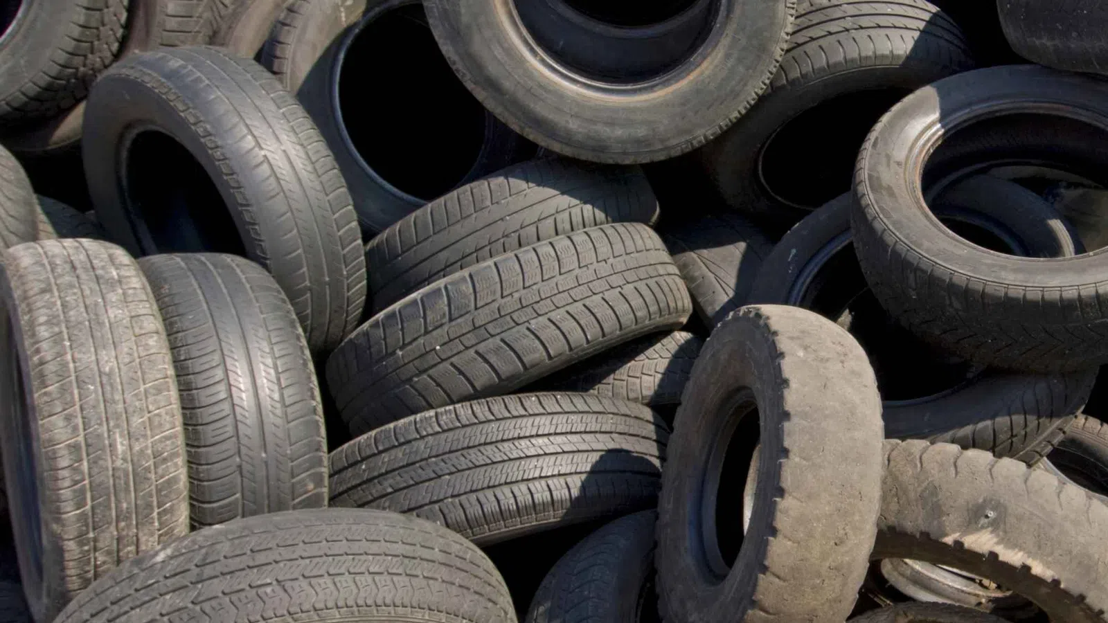 Pile of used black car tires stacked outdoors ready for recycling or disposal
