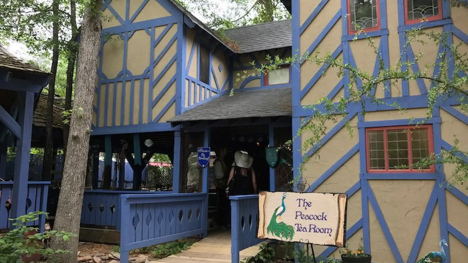 Rustic Tudor-style tea room with blue trim, surrounded by trees and a wooden entrance path.