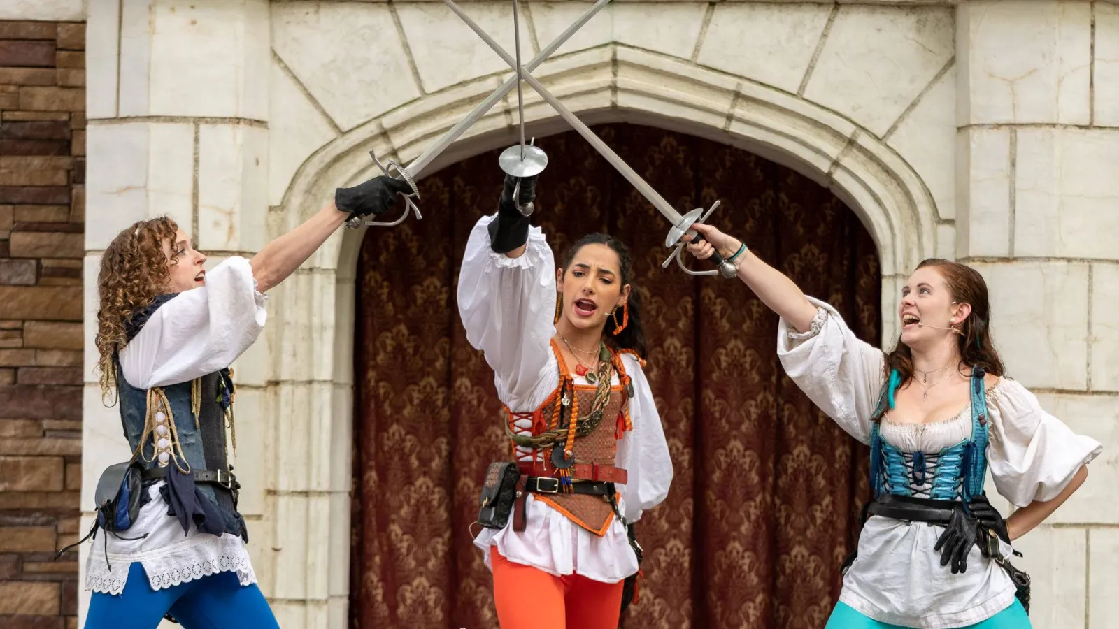 Three women in Renaissance costumes fence with swords