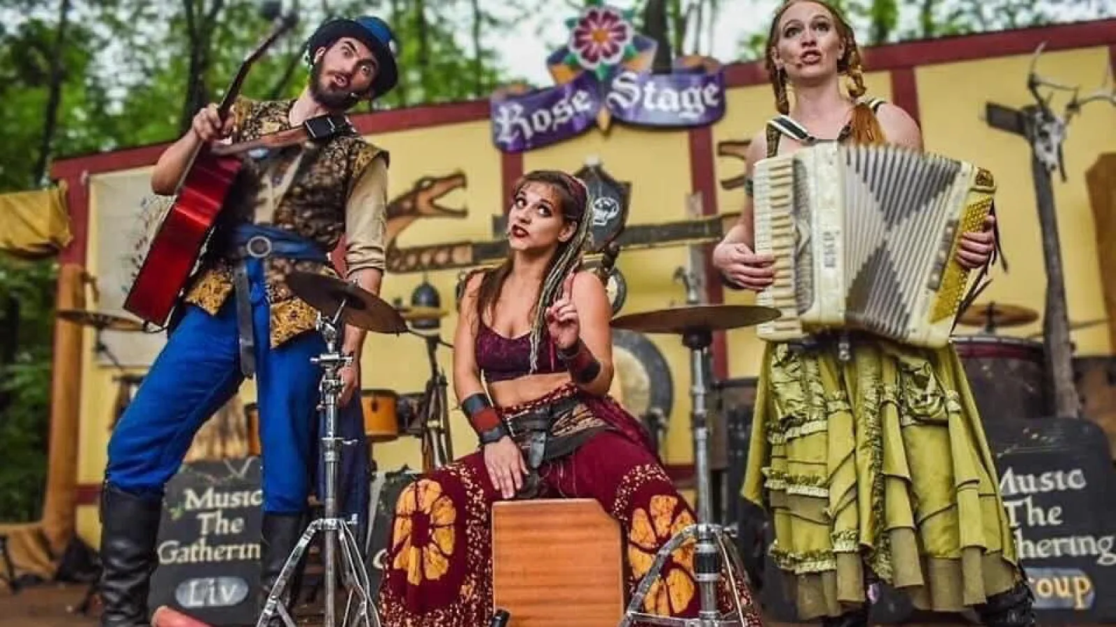 Three musicians performing on Rose Stage with guitar, accordion, and percussion