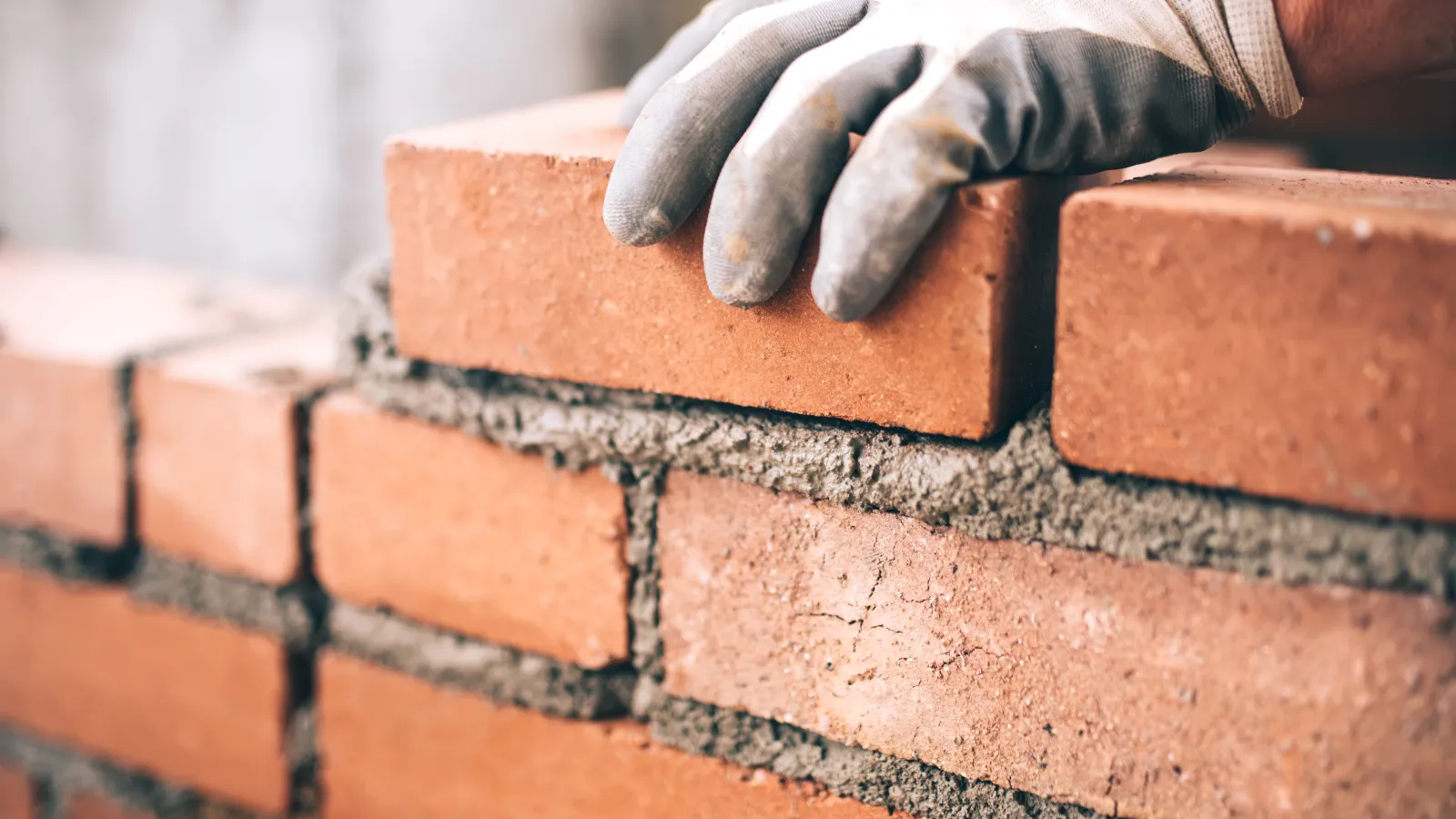 Worker wearing gloves laying red bricks with cement mortar in close-up of bricklayer construction