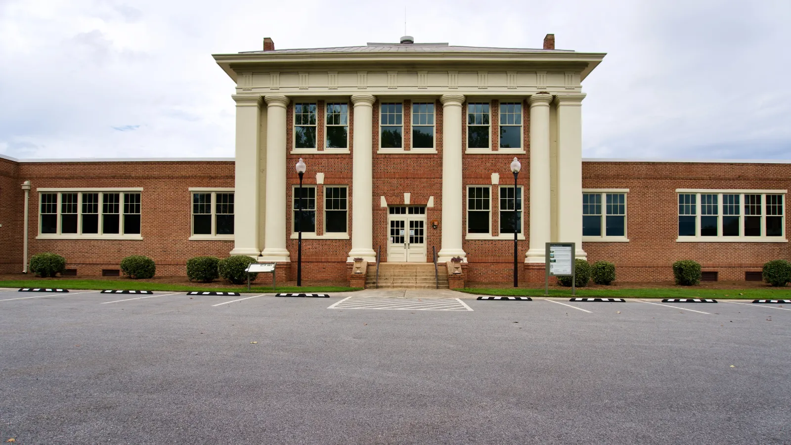 Classic red brick school building with large white columns and symmetrical windows on an overcast day