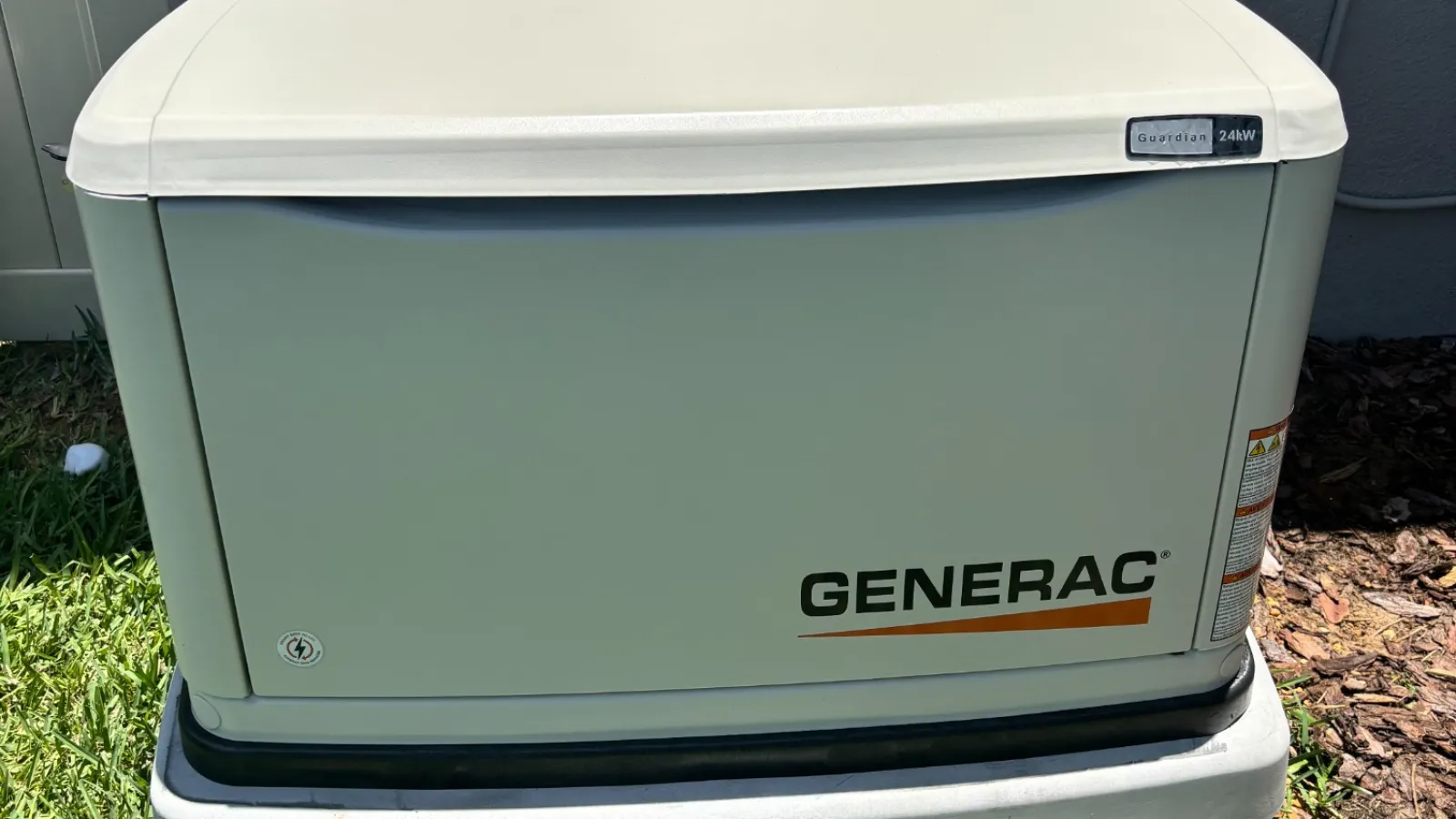 Generac standby generator installed outdoors on a concrete base beside a house with grass and mulch nearby