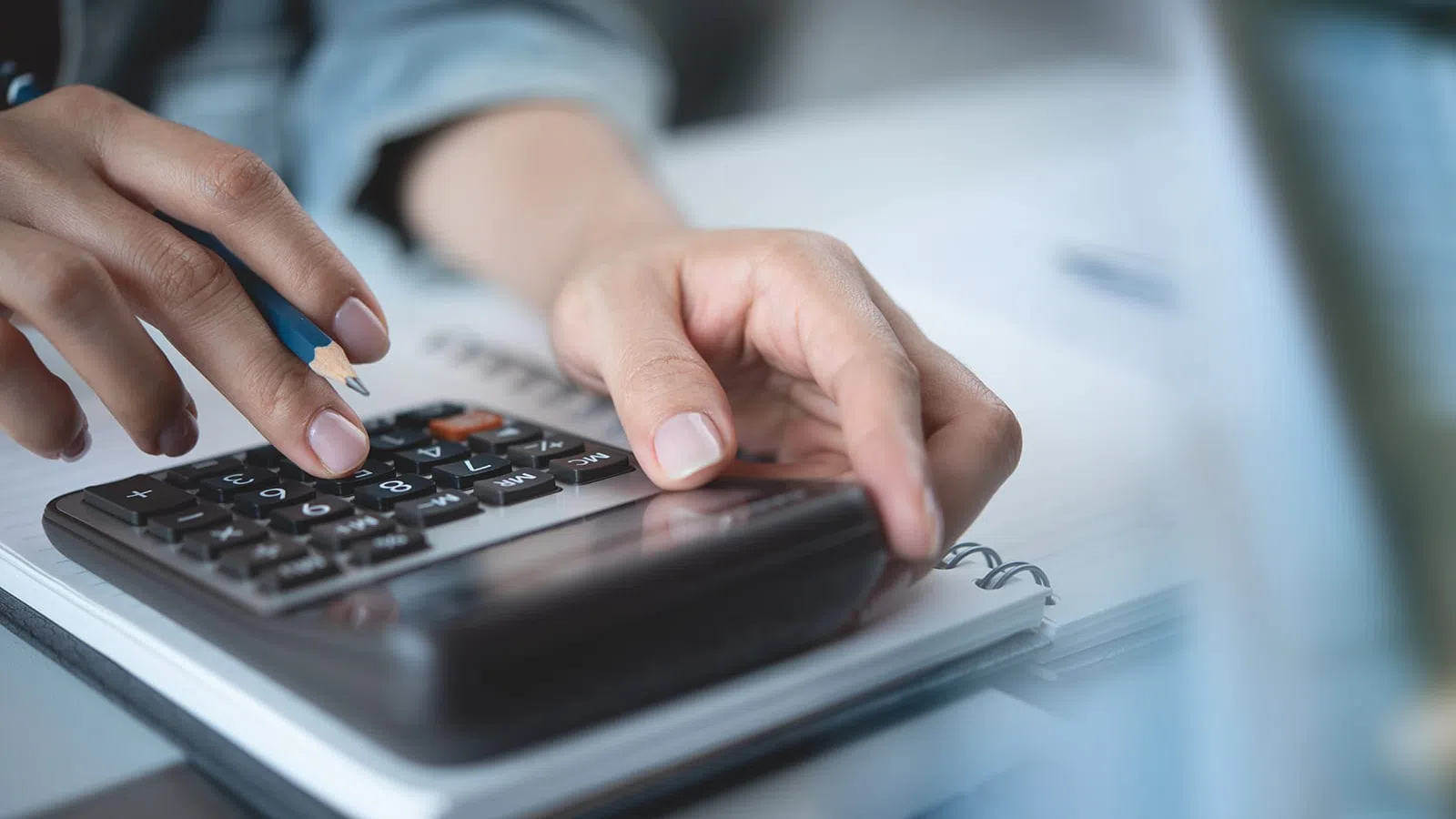 Close-up of hands using a calculator and pencil to perform financial calculations on a notebook.