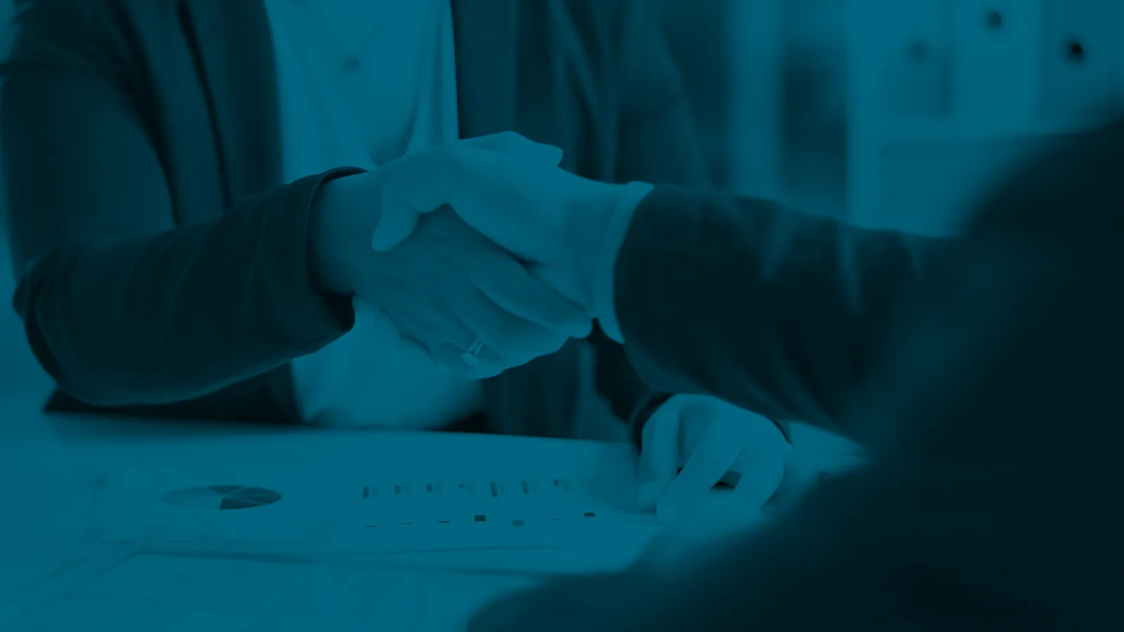 Two business professionals shaking hands over documents during a meeting to finalize an agreement.