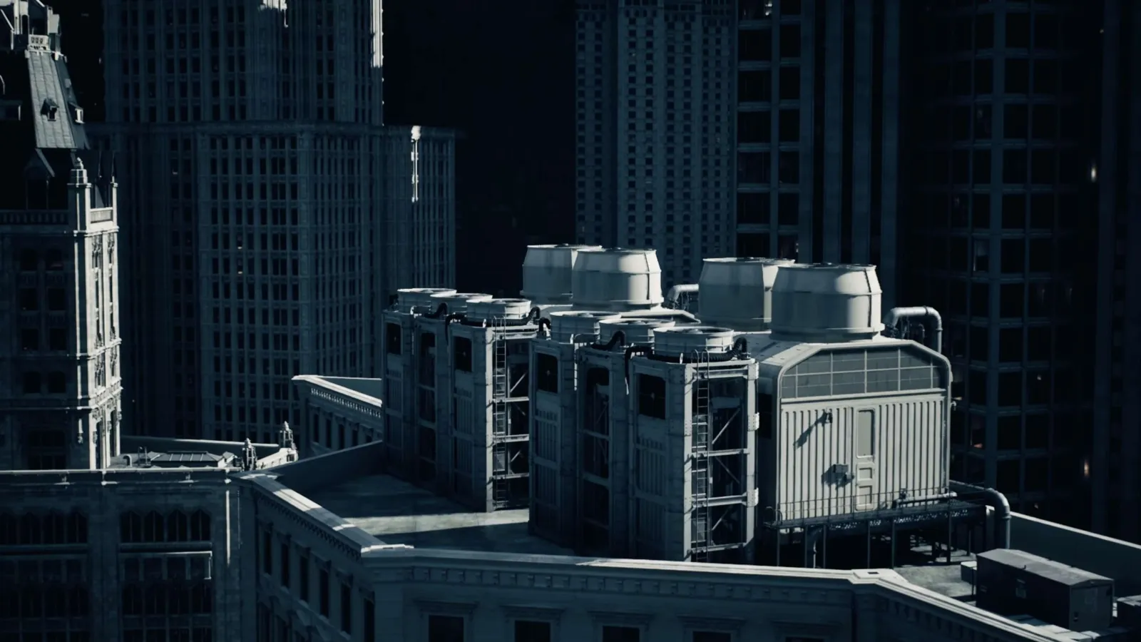 Rooftop industrial HVAC units on top of a city building surrounded by high-rise skyscrapers in shadows.
