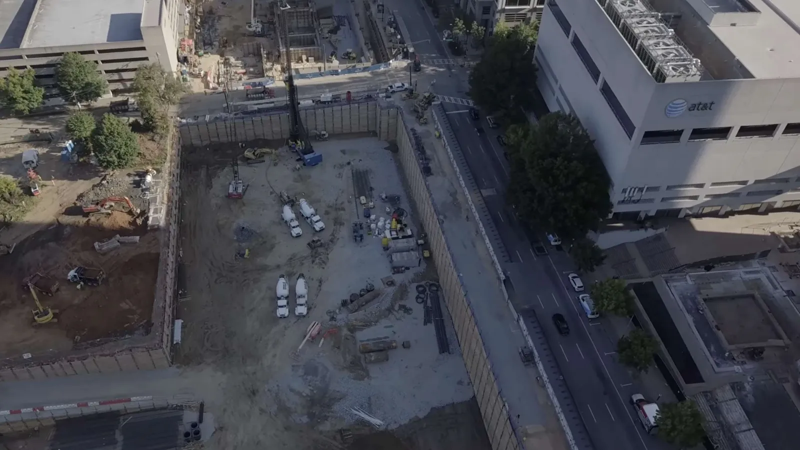 Aerial view of an urban construction site with machinery, excavated earth, and surrounding buildings under daylight.