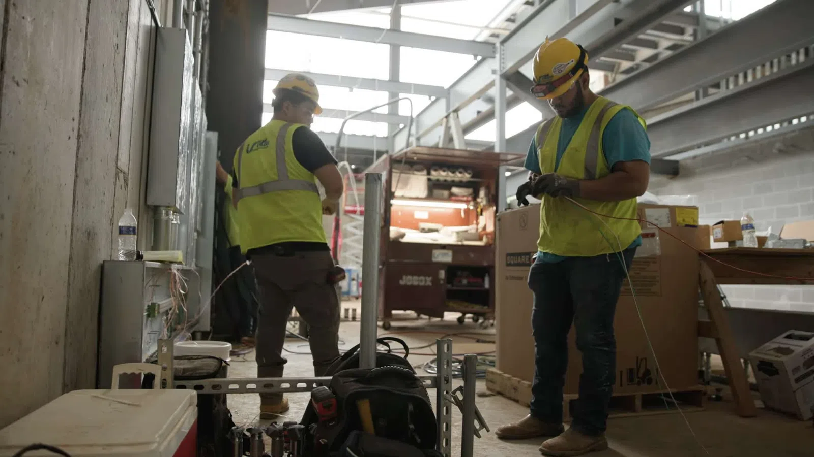 Two construction workers in safety vests and helmets working with tools inside a building under construction.