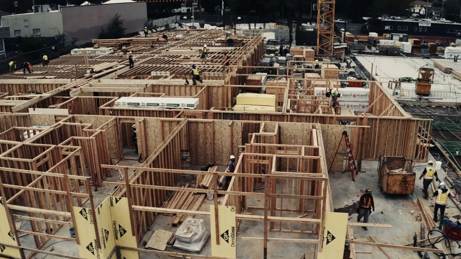 Aerial view of wooden frame construction site with workers building a large residential structure.