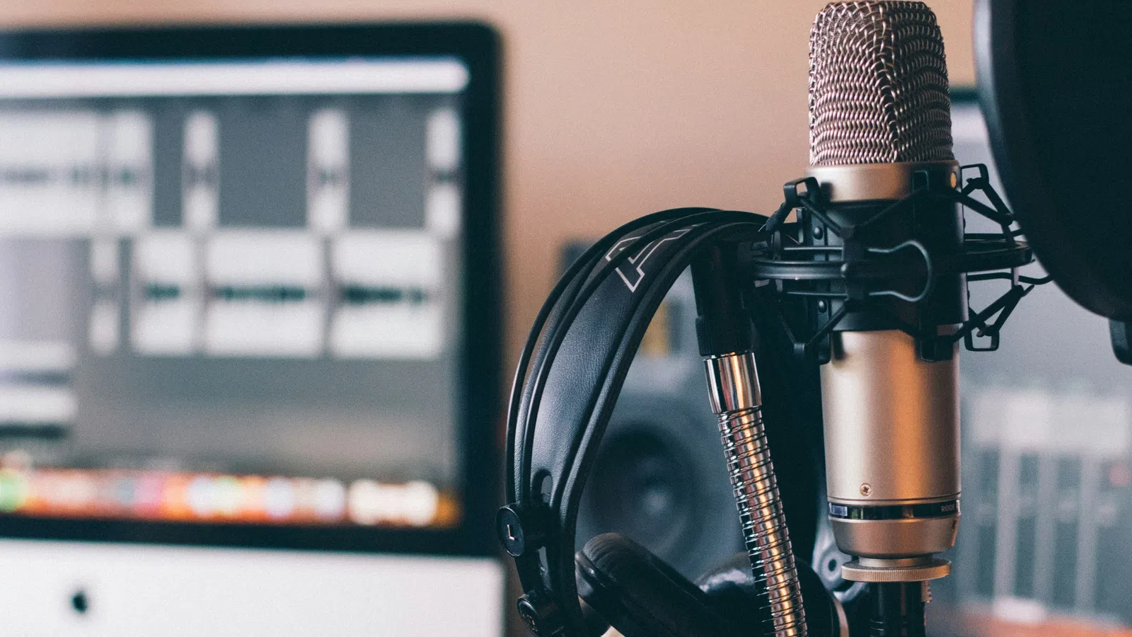 Studio microphone and headphones in front of a computer screen displaying audio editing software.