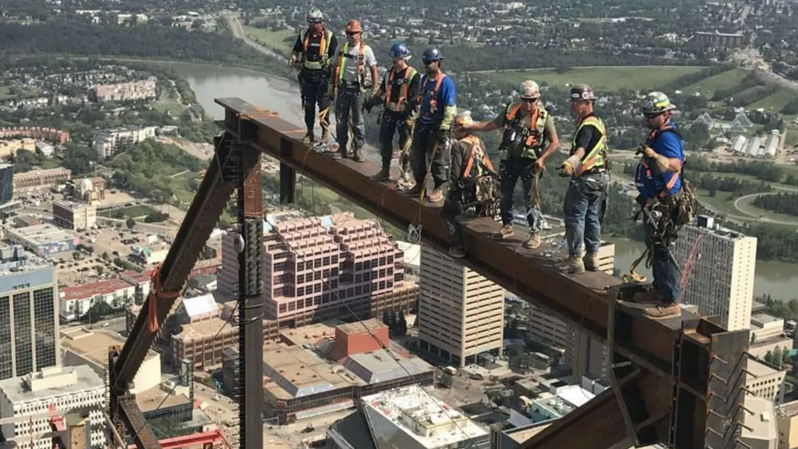 Workers in safety gear guiding heavy machinery lifting large industrial gear outdoors at construction site.