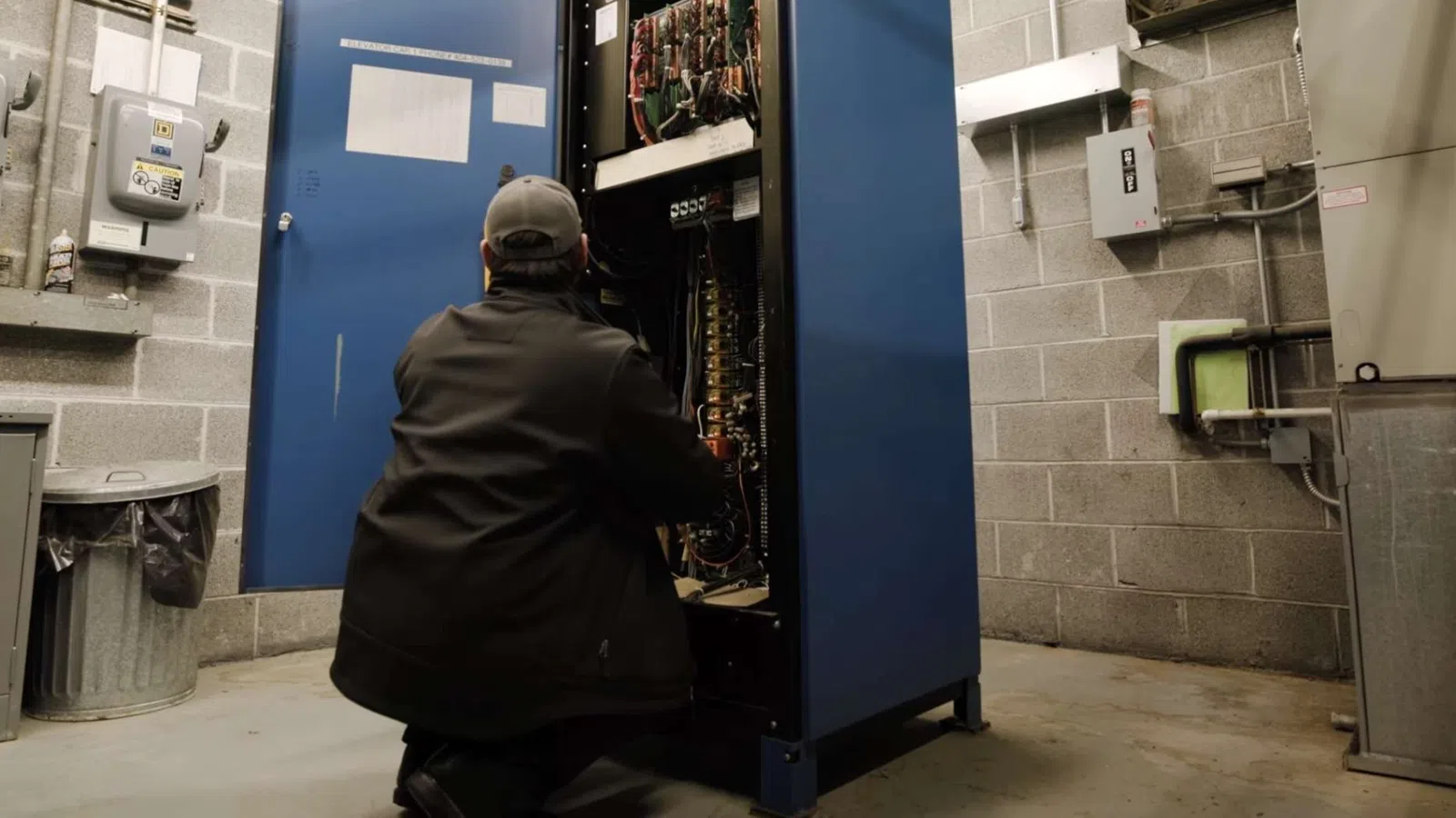 Electrician wearing yellow helmet fixing colorful wires in electrical control panel with circuit breakers.