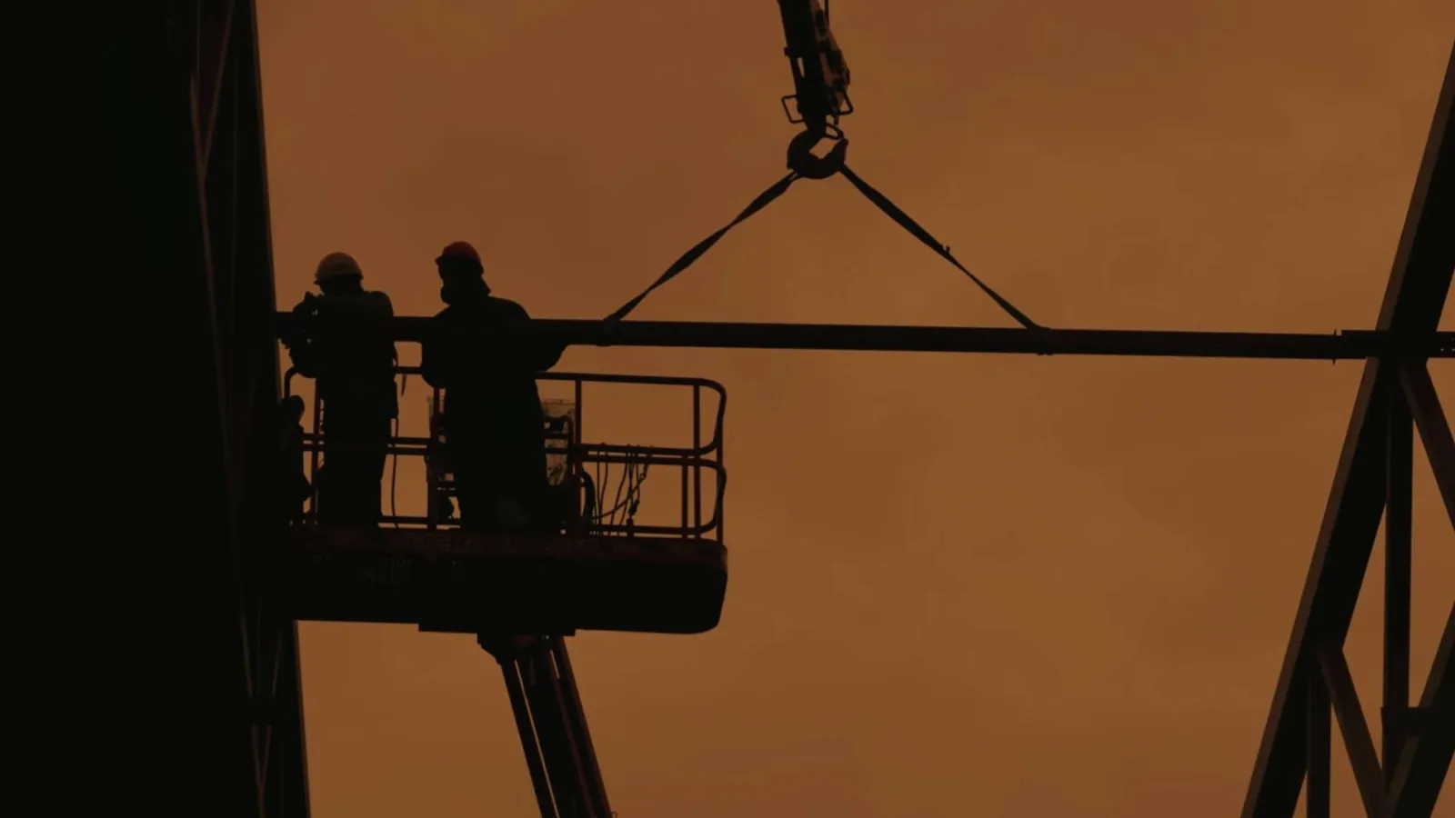 Workers in safety gear install large glass panels with city skyline and Ferris wheel reflections on a sunny day.