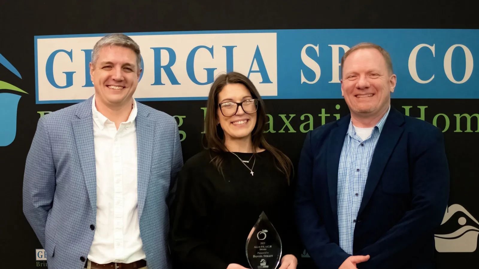 Three professionals smiling in front of Georgia SPC Co. banner, one holding an award trophy