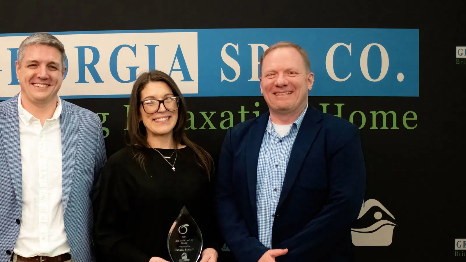 Three professionals smiling in front of Georgia SPC Co. banner, one holding an award trophy