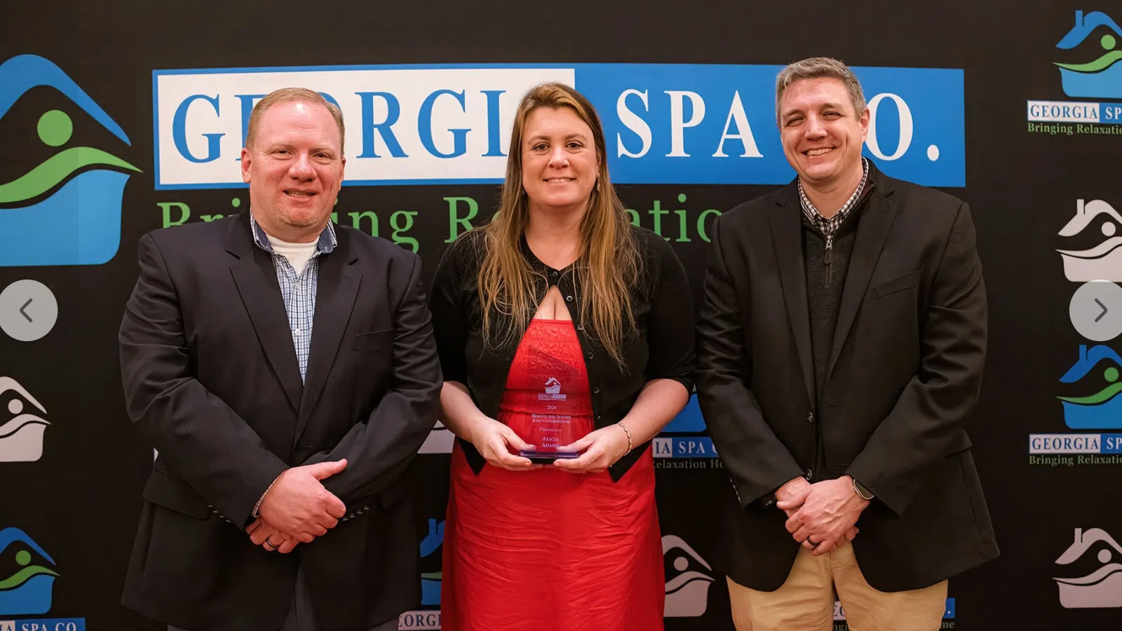 Three people standing in front of Georgia Spa Co. banner with woman in red dress holding an award plaque