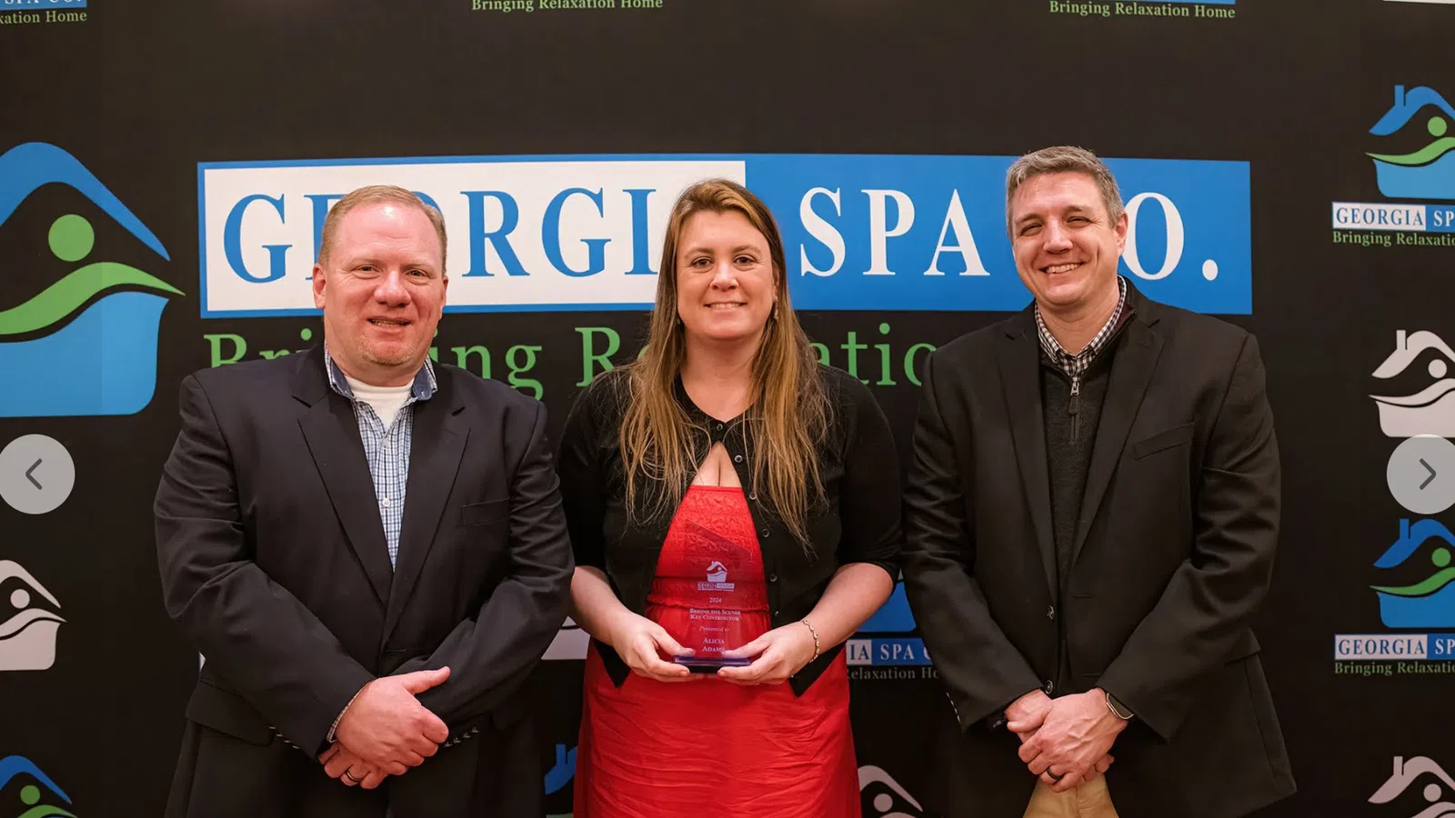 Three people standing in front of Georgia Spa Co. banner with woman in red dress holding an award plaque