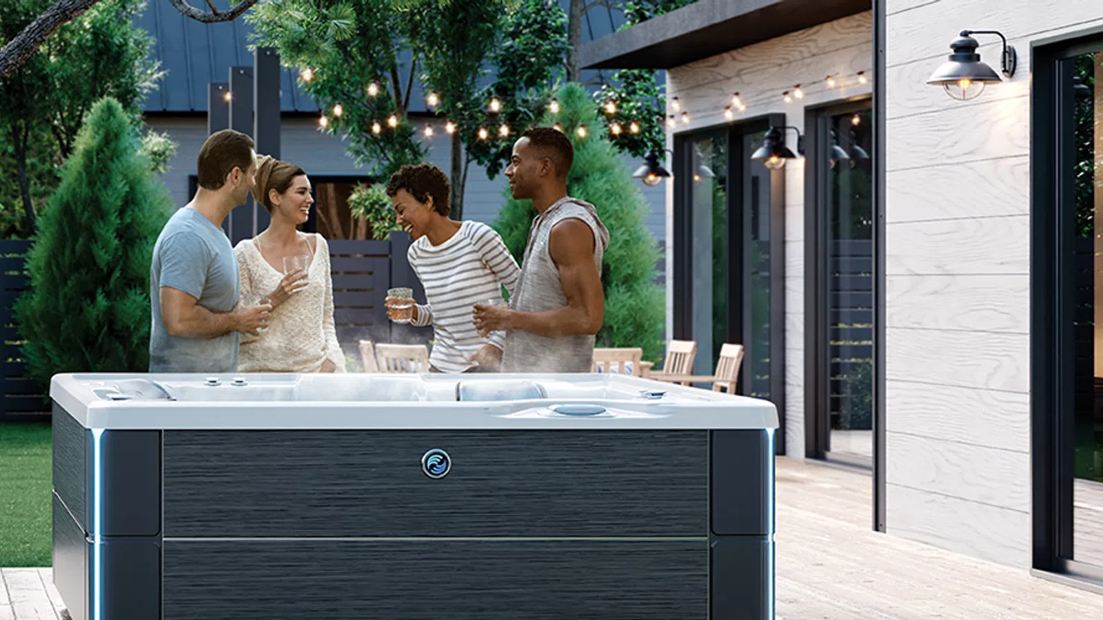 Four friends chatting and enjoying drinks around a hot tub on a modern outdoor patio with trees and garden.