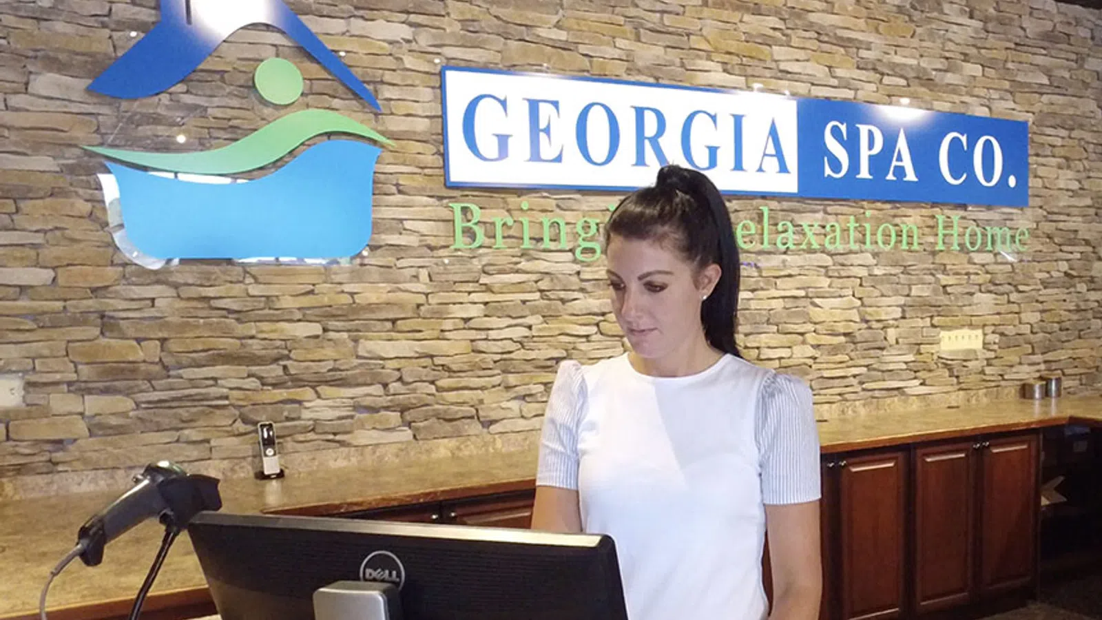 Receptionist at Georgia Spa Co. standing at counter with stone wall and company sign behind her