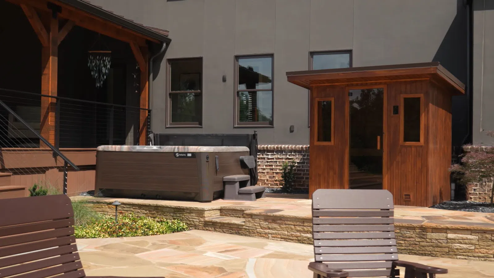 Modern backyard patio with stone flooring, wooden chairs, hot tub, and an outdoor sauna.