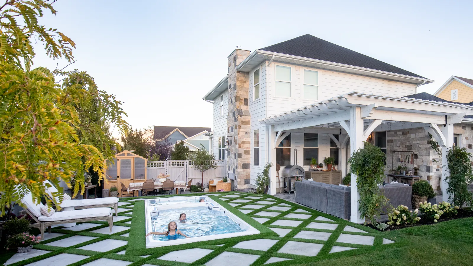 Modern backyard with swim spa, white pergola, outdoor seating, and manicured grass and stone pathway.