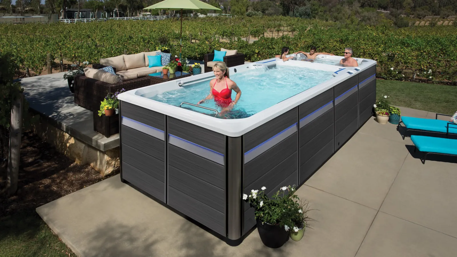 Outdoor swim spa with people enjoying water exercise and relaxation in a backyard patio with greenery.