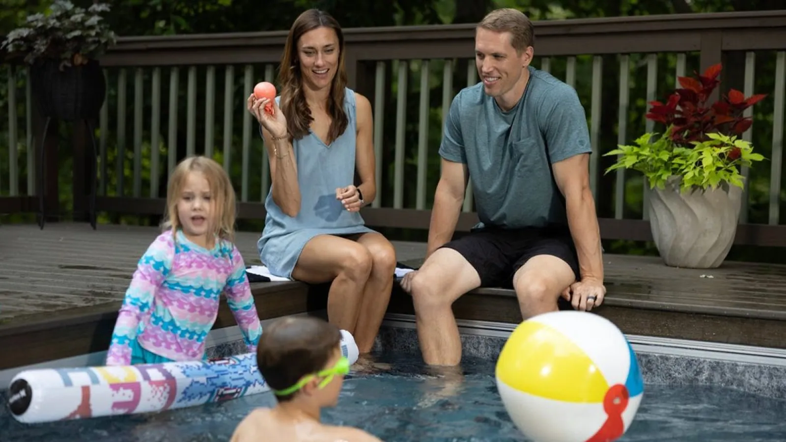 Family enjoying time by the pool with children playing and parents sitting on deck relaxing.